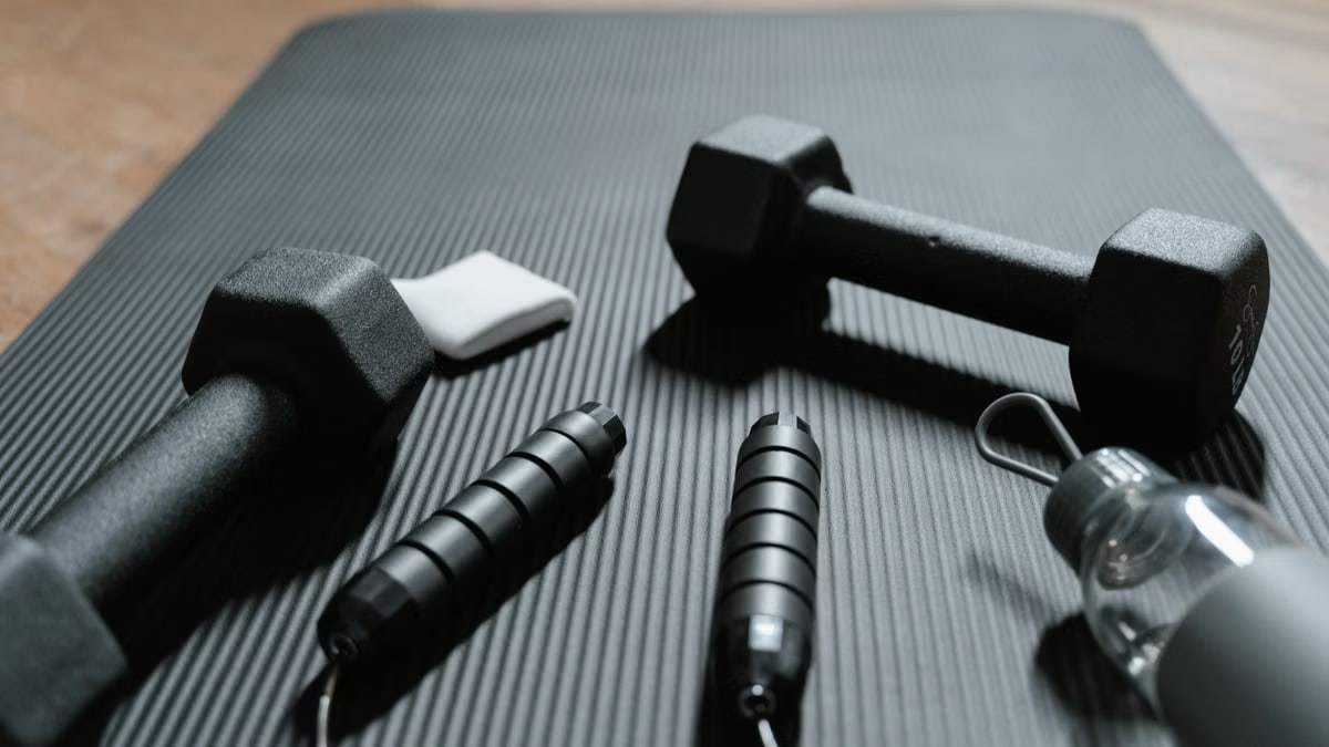 Close-up of dumbbells, jump rope, and water bottle on a yoga mat, ideal for home fitness routines.
